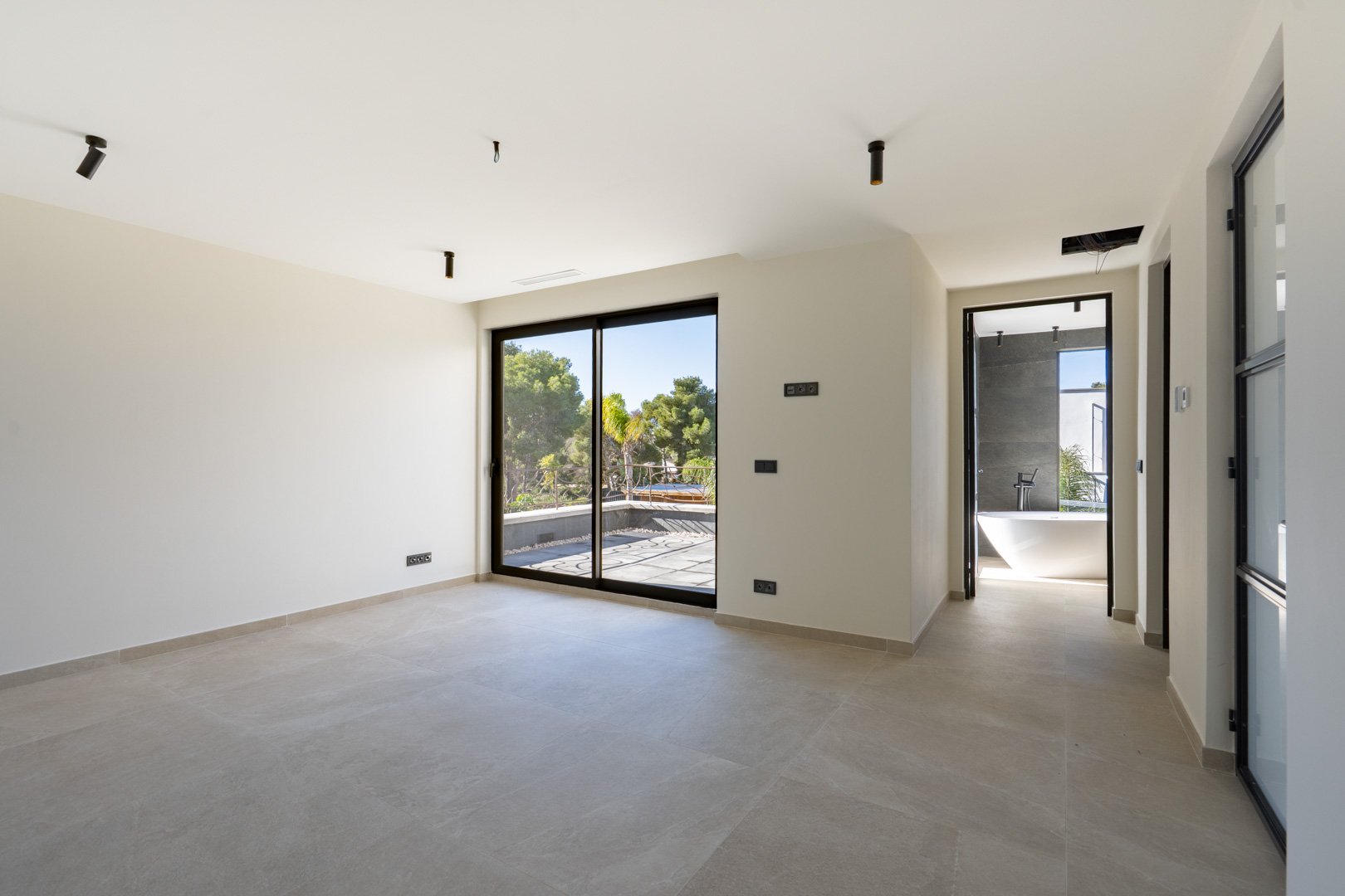 Dormitorio principal con acceso a terraza privada, suelos cerámicos y baño en suite con bañera exenta y revestimientos en gris antracita.