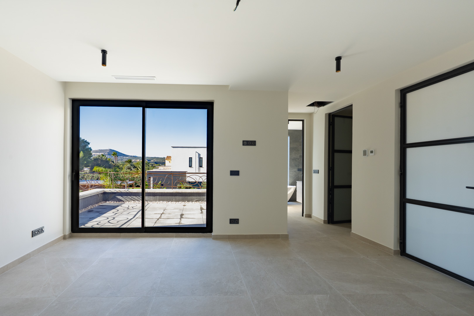 Dormitorio principal con acceso directo a terraza privada, suelos de gres porcelánico y carpintería negra. Se aprecia el baño en suite con bañera exenta.