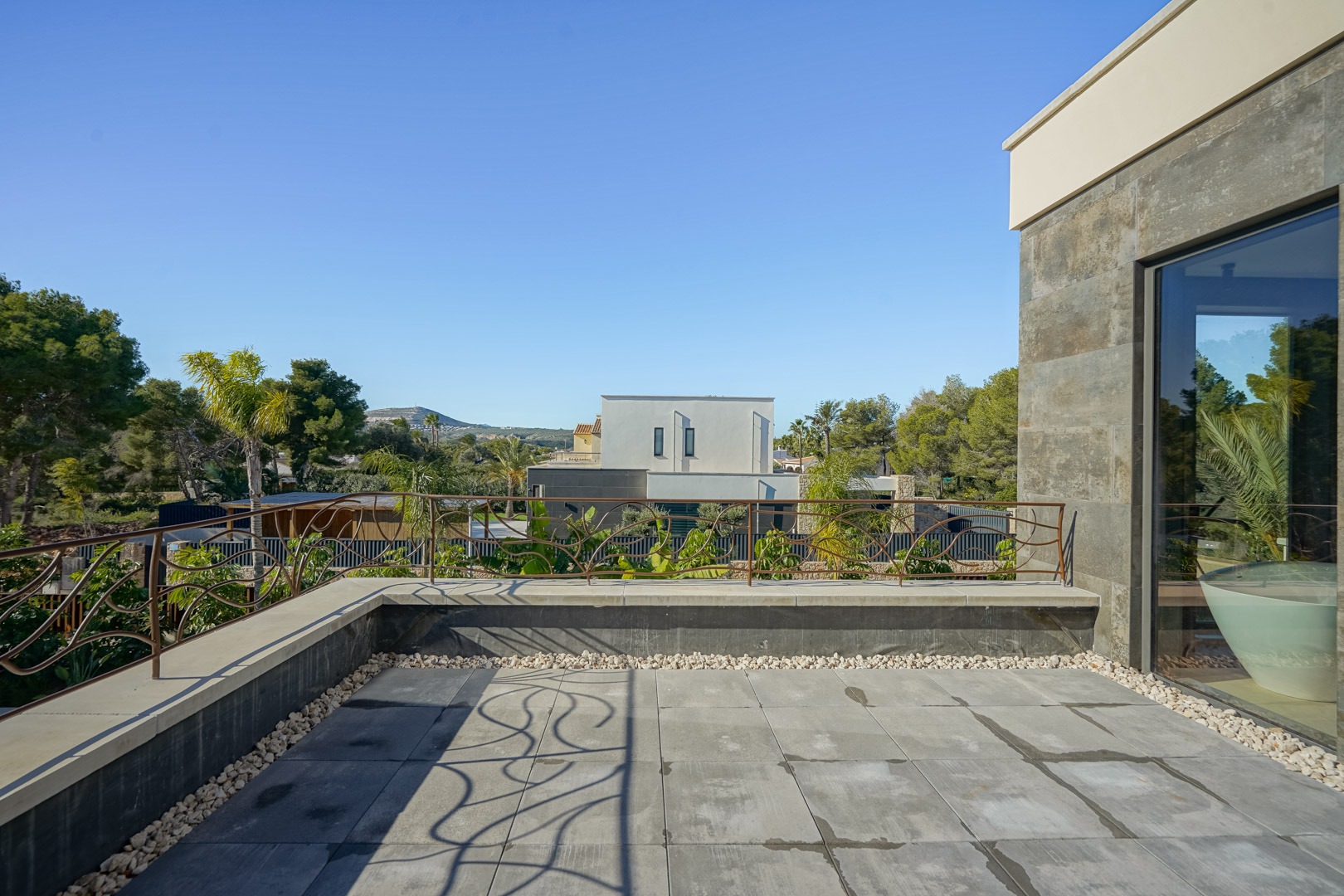 Terraza privada en la planta superior con suelo de gres gris, barandilla de diseño orgánico y vistas despejadas al entorno natural de Jávea.