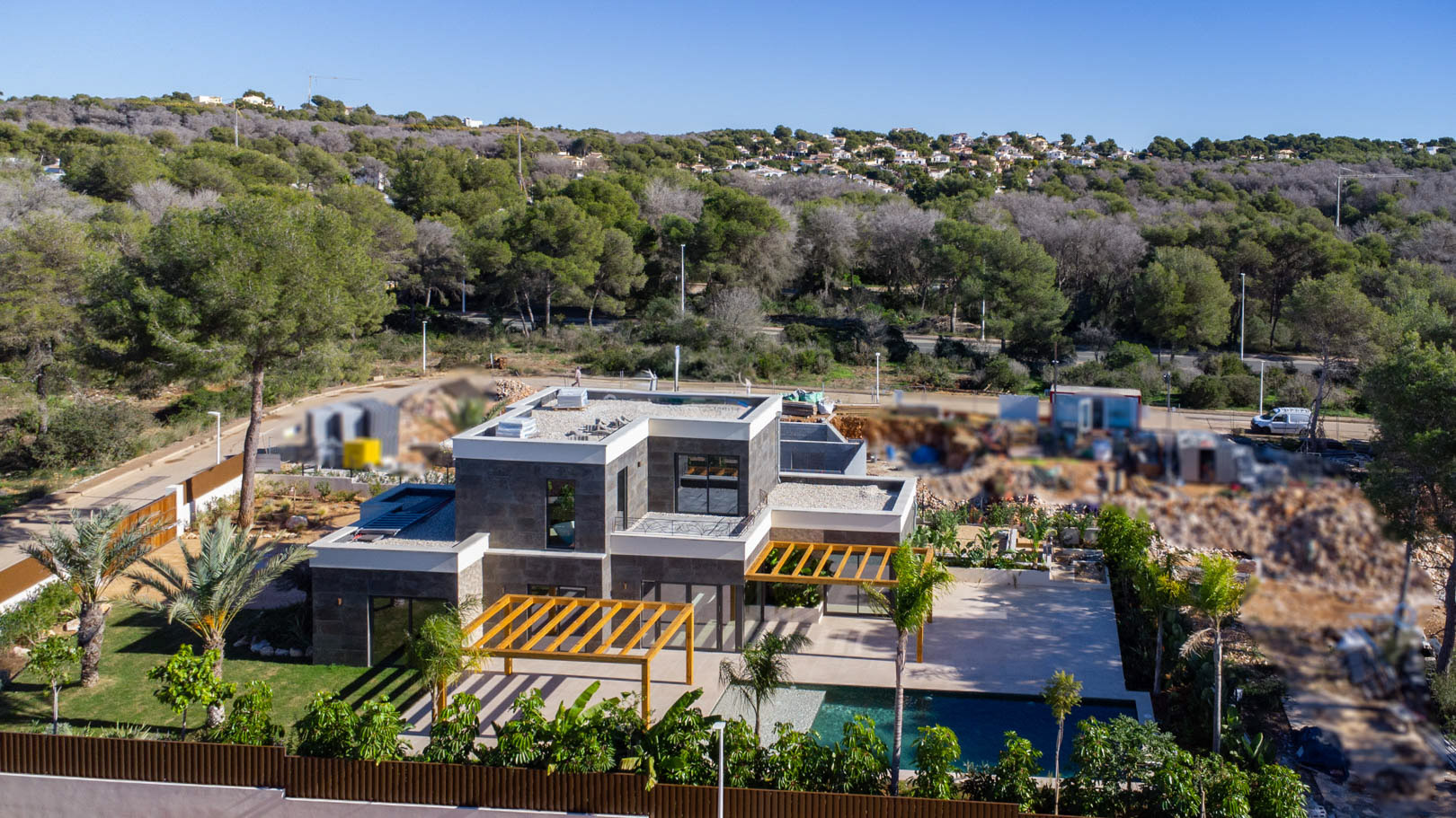 Vista aérea de la villa con fachada de piedra oscura, pérgolas de madera de iroko y piscina de estilo Bali, rodeada de un jardín mediterráneo y bosque.