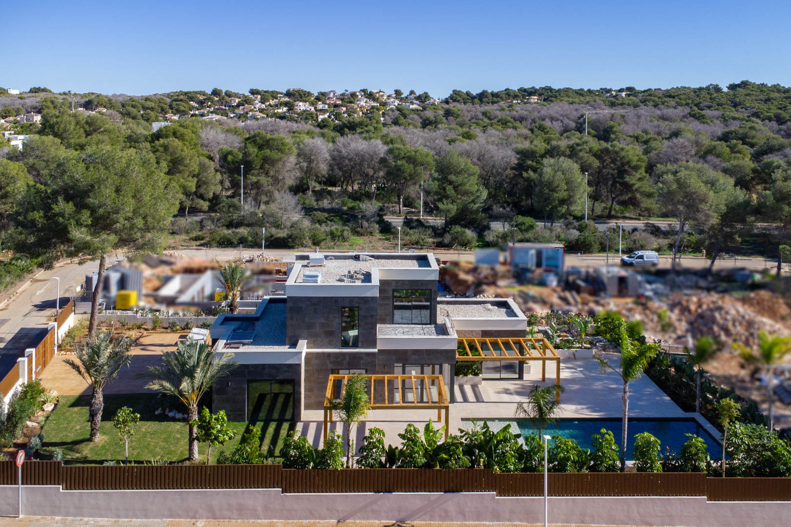 Vista aérea de la villa moderna con fachada de piedra, pérgolas de madera de iroko, piscina de estilo Bali y jardín mediterráneo rodeado de naturaleza.