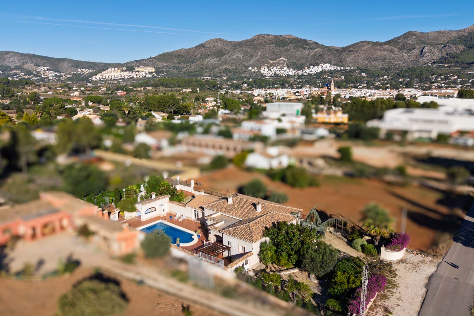 Vista aérea de la villa con tejado de teja y piscina privada, rodeada de vegetación y con vistas panorámicas al pueblo de Jalón y las montañas.