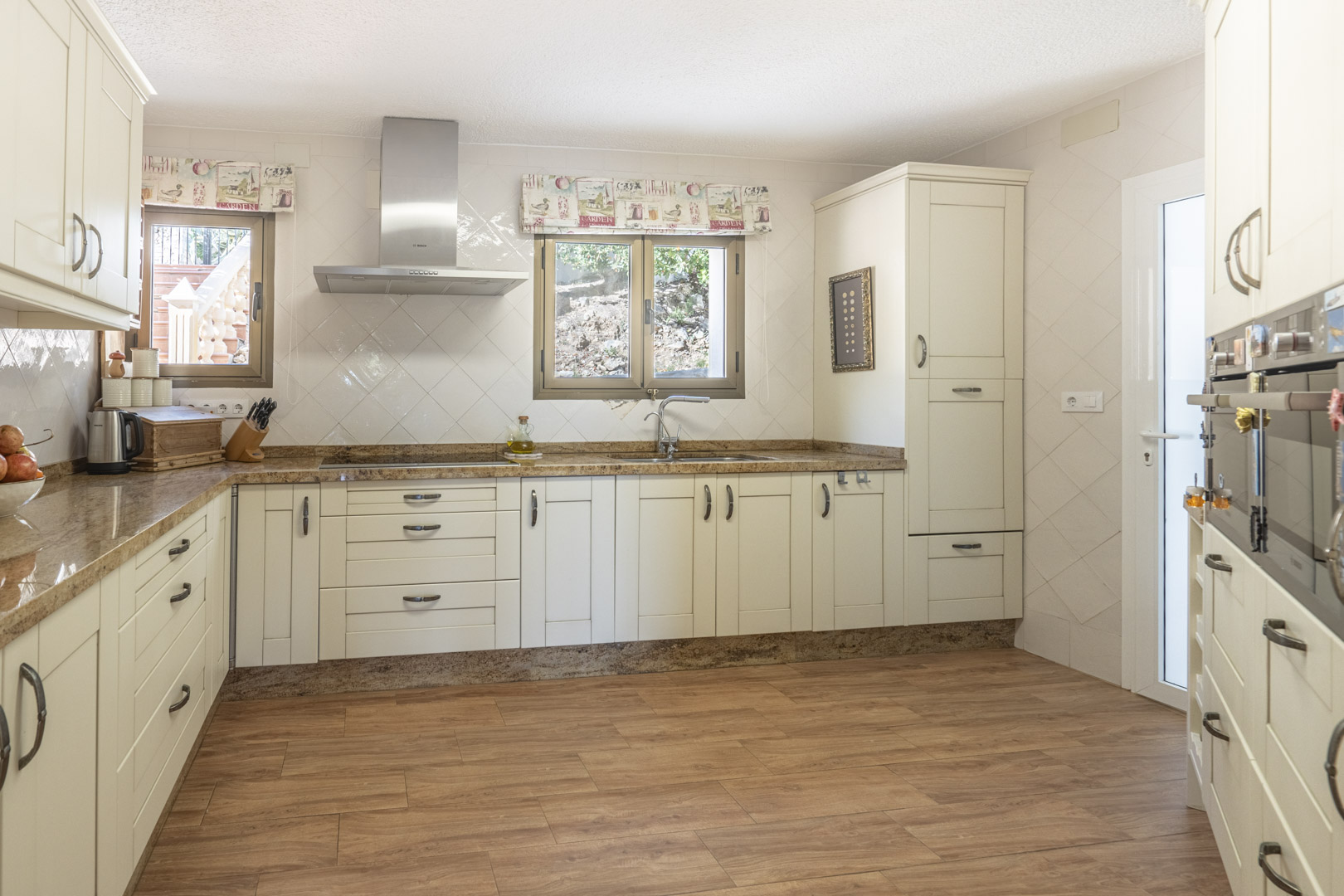 Cocina renovada con mobiliario color crema, encimeras de granito, campana extractora de acero inoxidable y suelos cerámicos con acabado efecto madera.