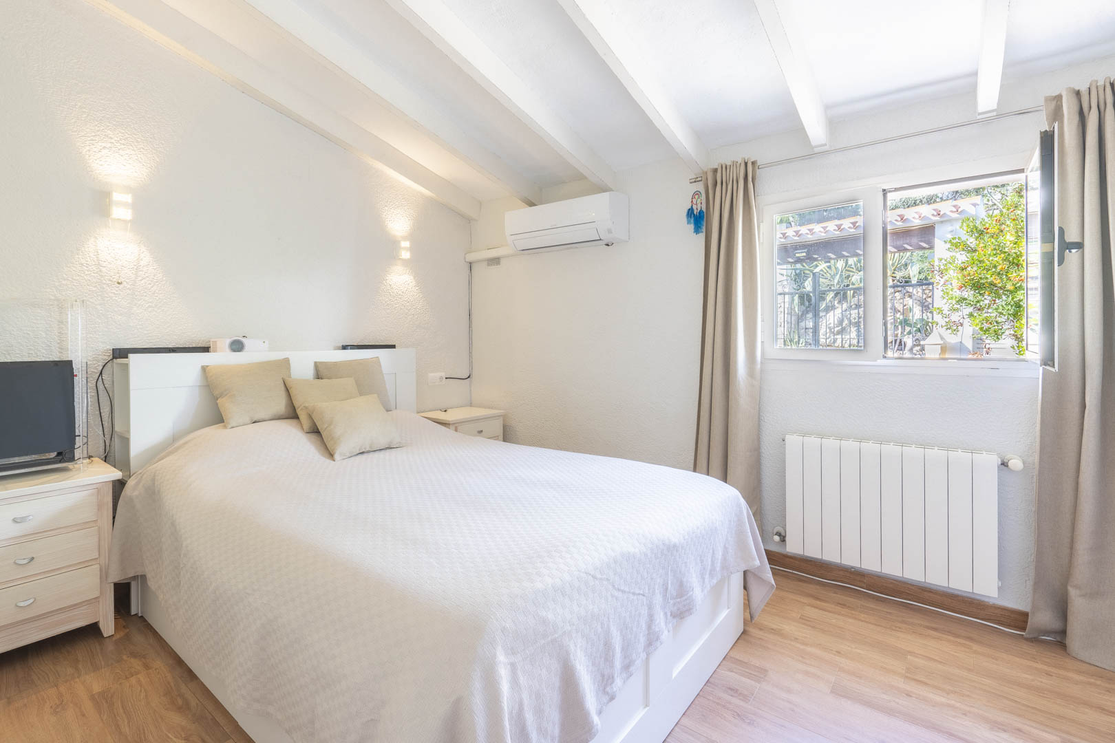 Dormitorio con techo de vigas blancas, aire acondicionado y calefacción por radiador. Dispone de suelos laminados y ventana con vistas al exterior.