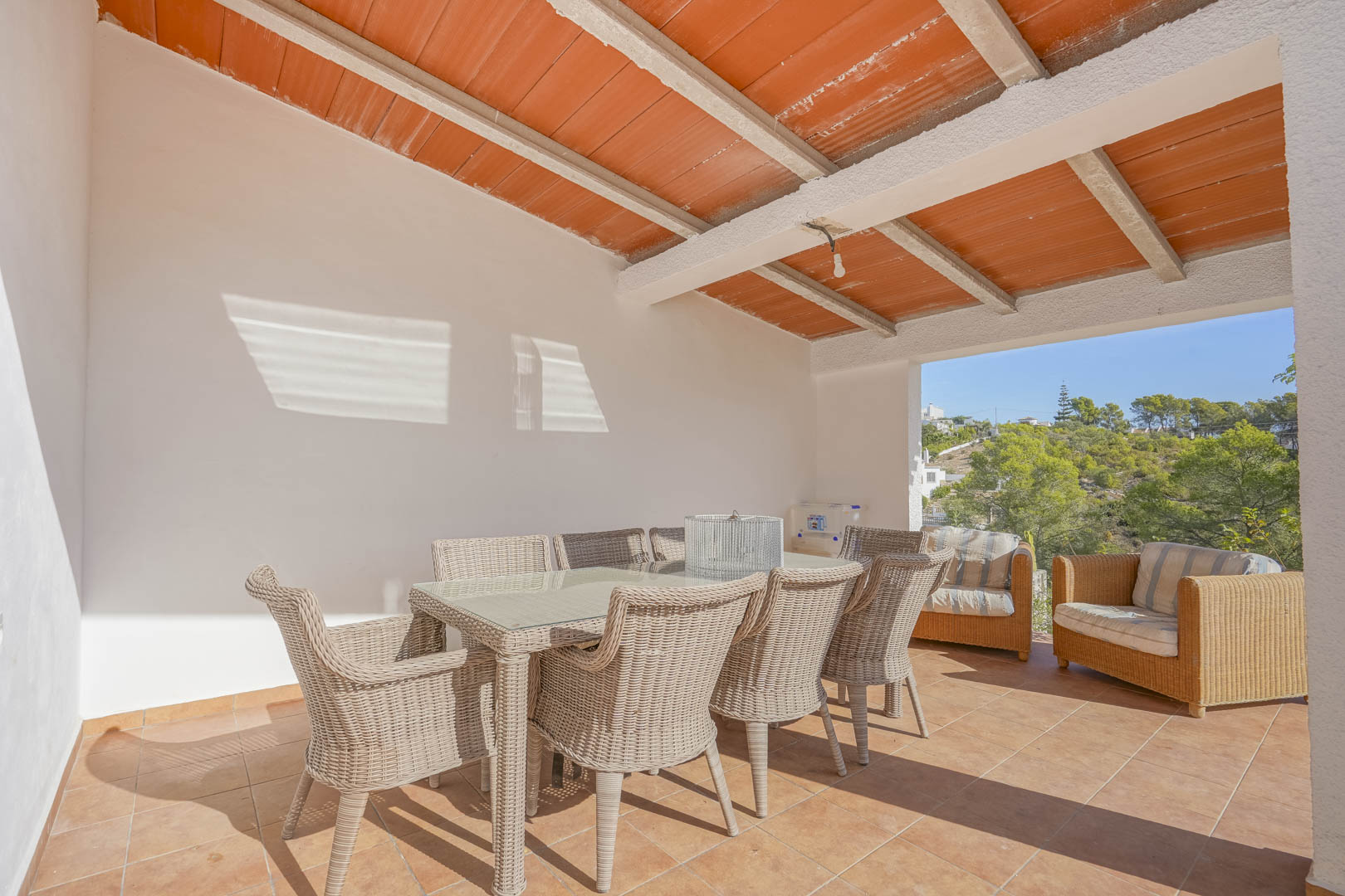 Terraza cubierta con vigas de hormigón y bovedillas cerámicas, equipada con comedor de mimbre y vistas despejadas al entorno natural de Jávea.