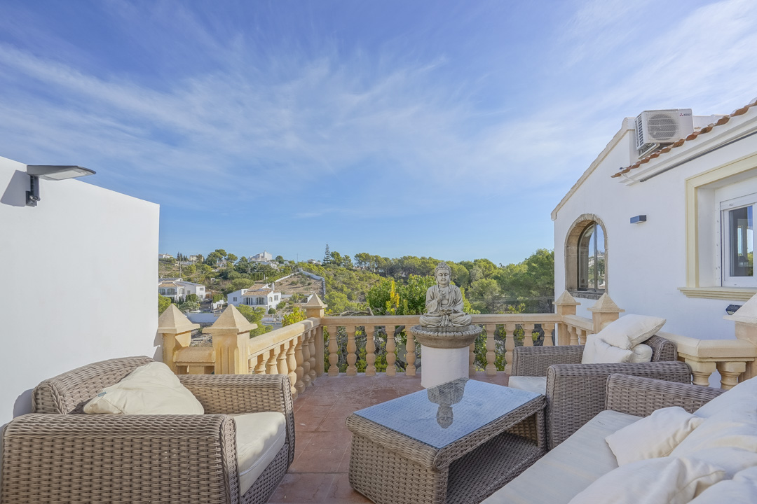 Terraza elevada con mobiliario de ratán, balaustrada de piedra tradicional y vistas despejadas al entorno natural y las colinas de Jávea.