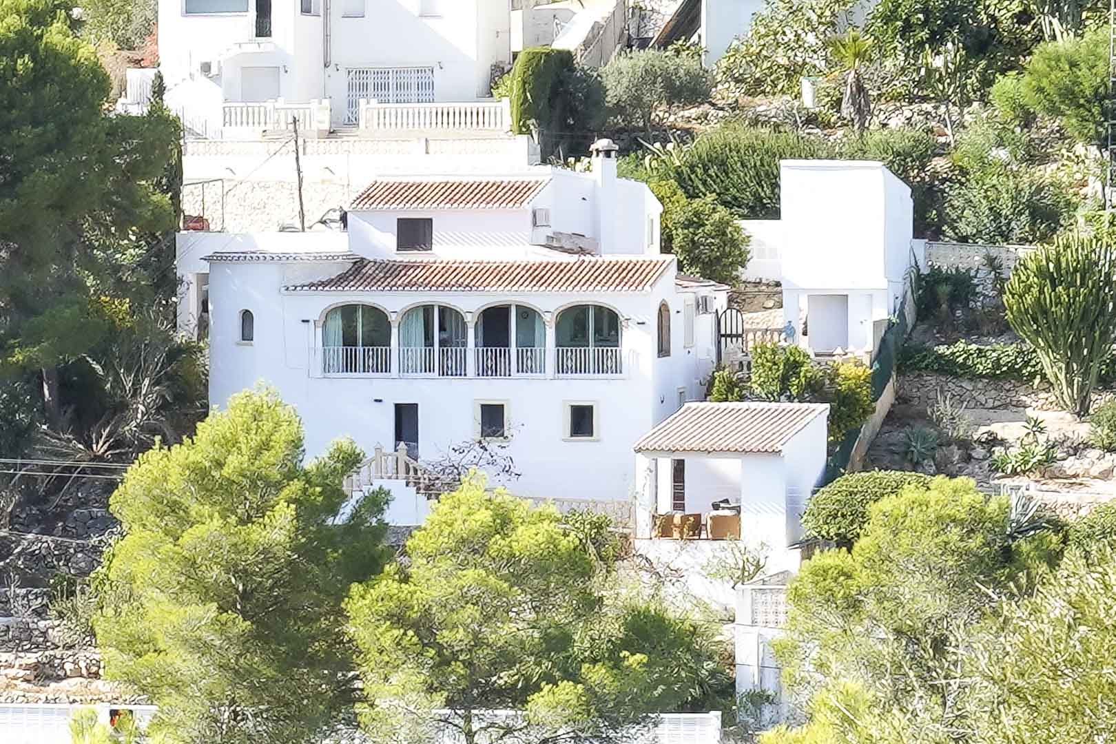 Vista exterior de la villa blanca con tejados de teja roja, destacando la naya de arcos tradicionales y su integración en el entorno natural de Pinomar.