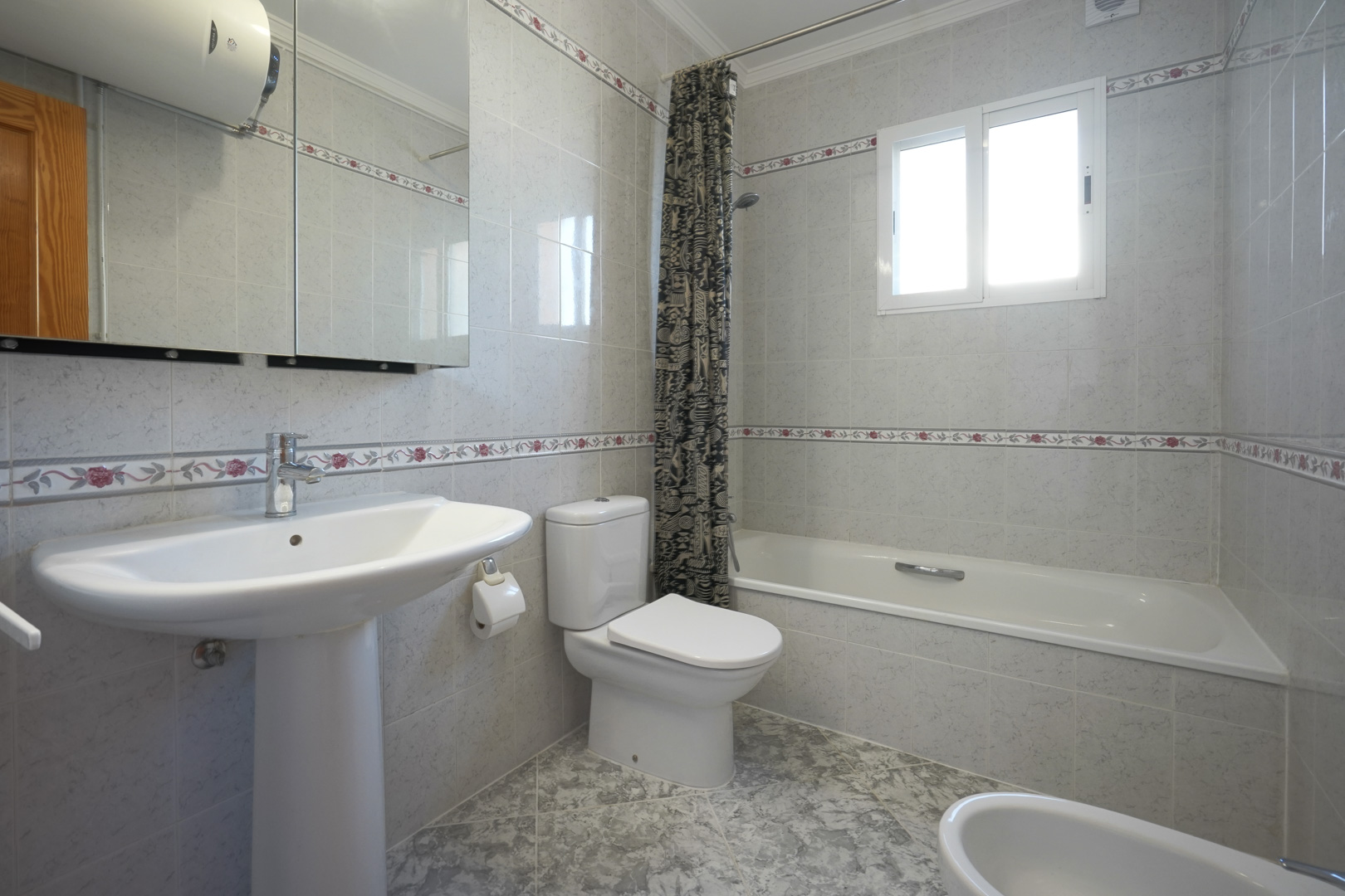 Cuarto de baño de estilo tradicional con paredes alicatadas y cenefa floral, equipado con bañera, lavabo de pedestal y armario de espejo.