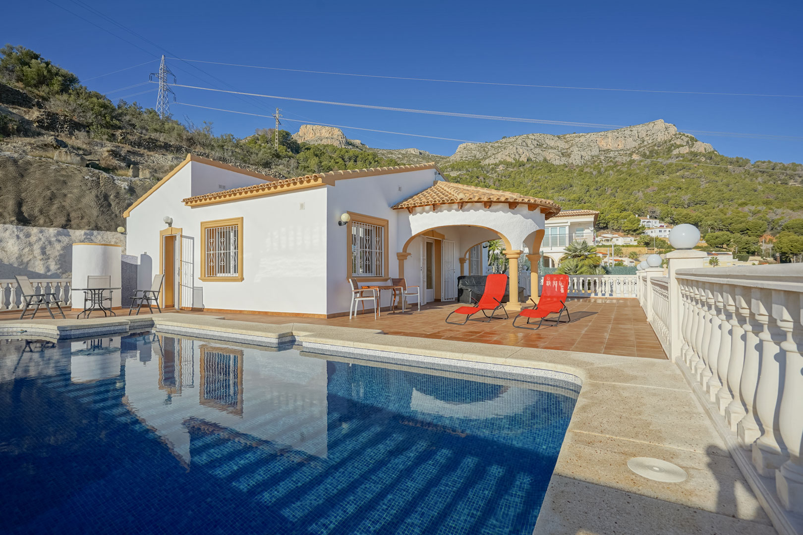 Exterior de la villa con piscina privada, amplia terraza de gres y porche arqueado tradicional, con la Sierra de Oltà como telón de fondo natural.