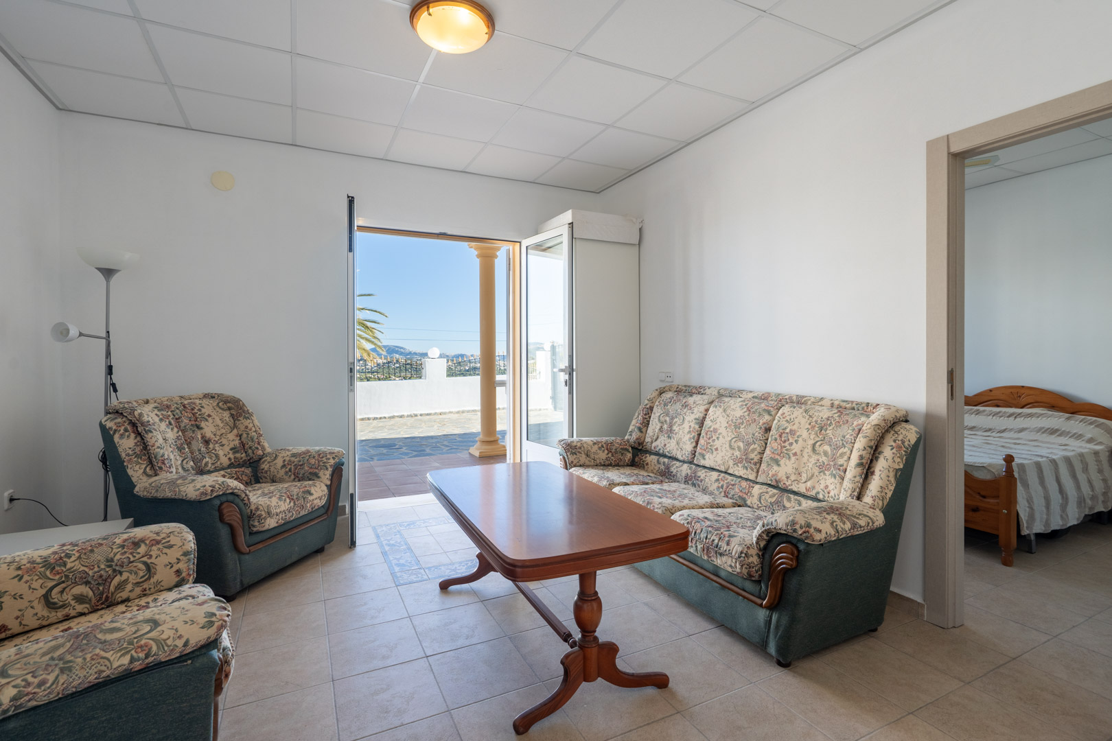 Salón del apartamento de invitados con sofás de estilo floral, mesa de centro de madera y acceso directo a la terraza exterior con vistas despejadas.
