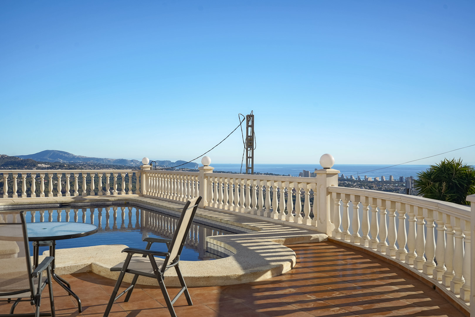 Terraza con piscina y balaustrada clásica que ofrece vistas panorámicas al mar Mediterráneo y al perfil urbano de Calpe bajo un cielo despejado.
