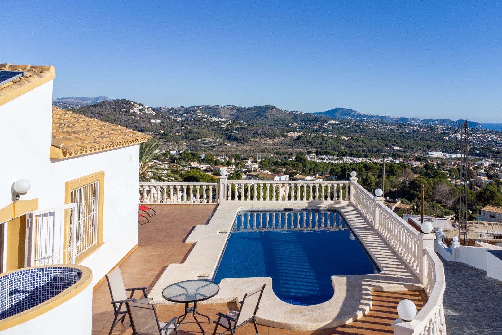 Terraza exterior con piscina, balaustrada clásica y vistas despejadas hacia la costa de Calpe y las montañas circundantes.