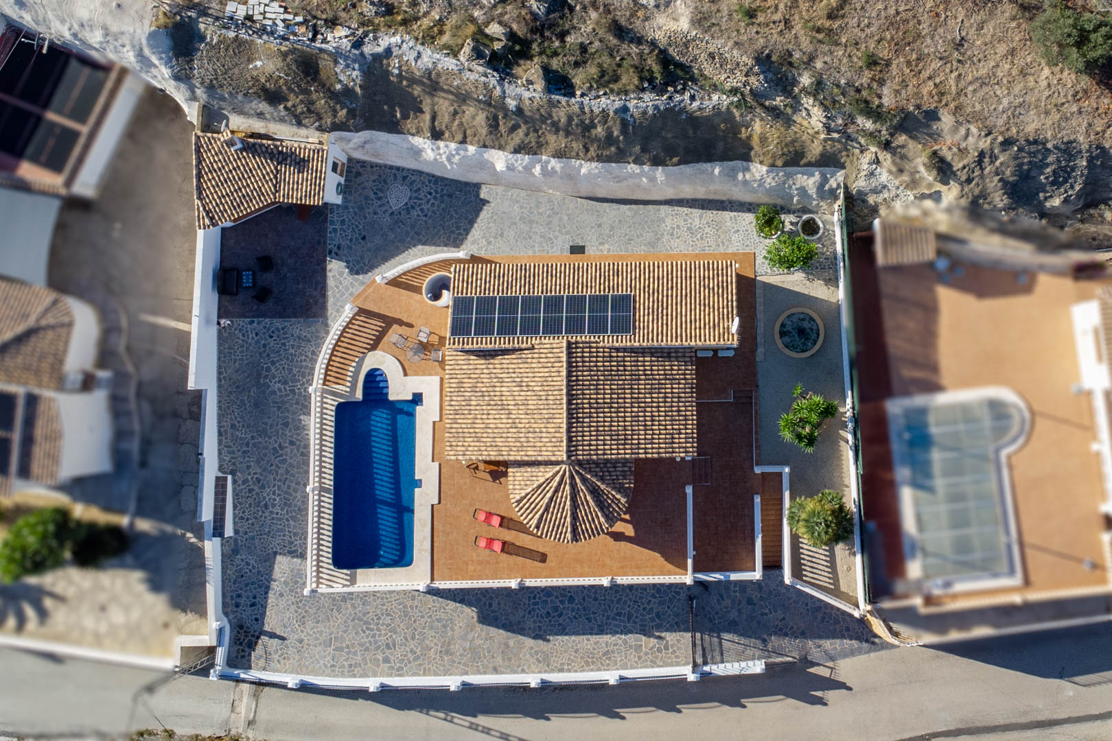 Vista aérea de la propiedad que muestra el tejado de teja con paneles solares, la piscina rectangular y las diversas áreas de terraza pavimentadas.