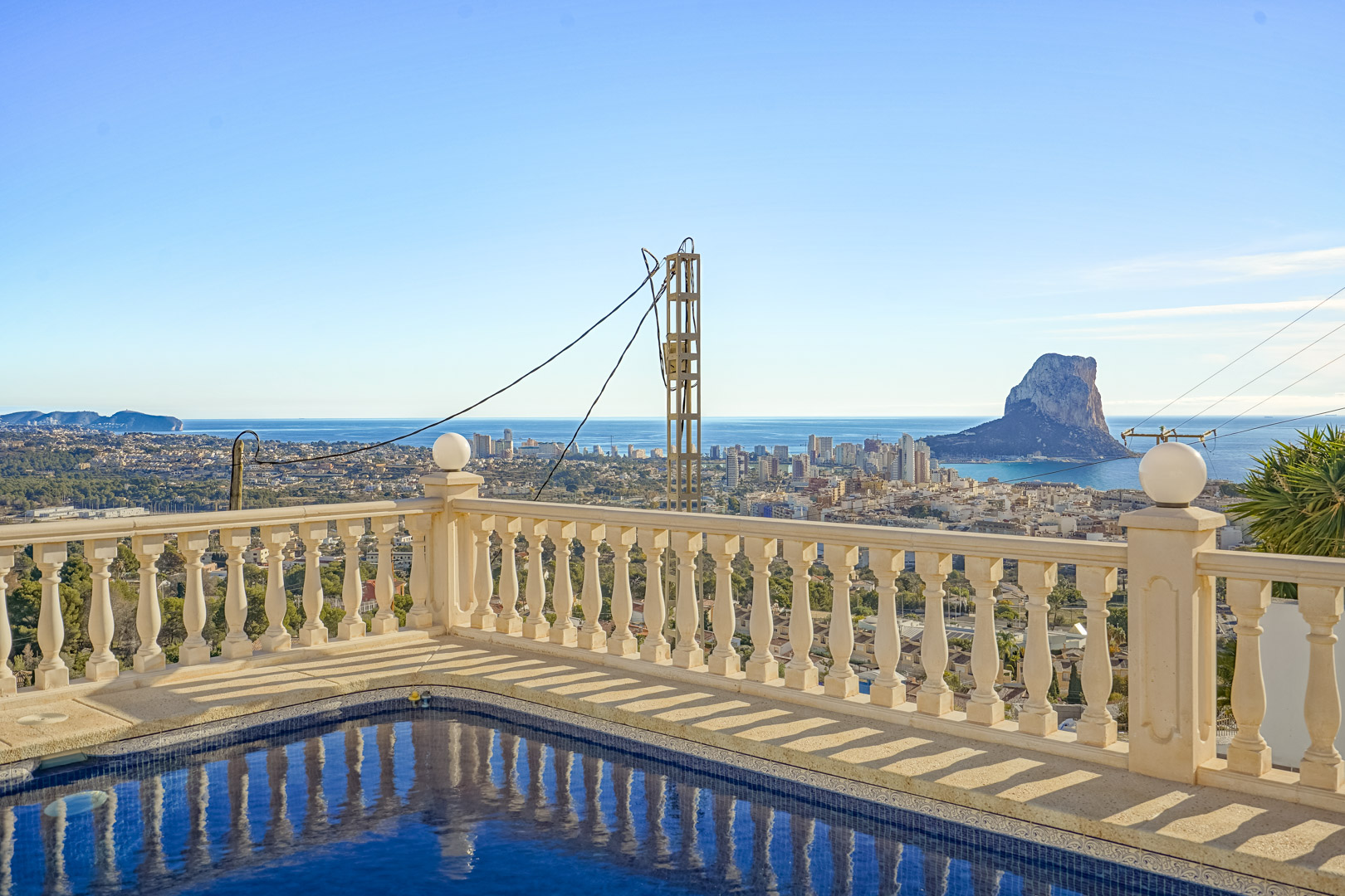 Vista desde la piscina con balaustrada clásica hacia el Peñón de Ifach, el skyline de Calpe y la costa mediterránea bajo un cielo despejado.