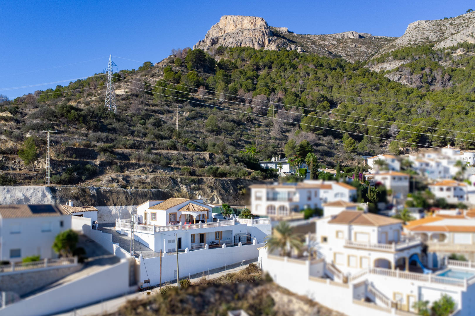 Vista exterior de la villa blanca situada en la ladera de la Sierra de Oltà, destacando su arquitectura tradicional con tejados de teja y amplias terrazas.