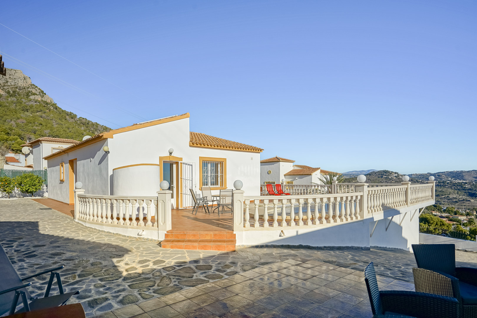 Vista exterior de la villa con amplia terraza de baldosas de terracota, balaustrada clásica y vistas panorámicas hacia la costa y la Sierra de Oltà.