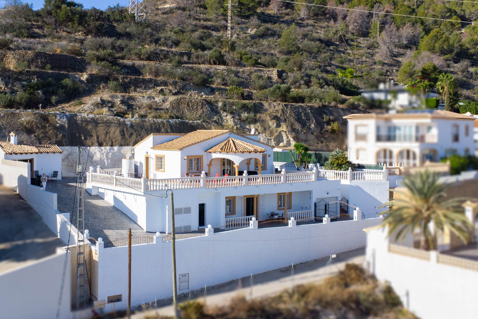 Vista exterior de la villa de dos niveles con fachada blanca, tejado de teja y amplias terrazas con balaustradas clásicas situadas en la ladera de la Sierra de Oltà.