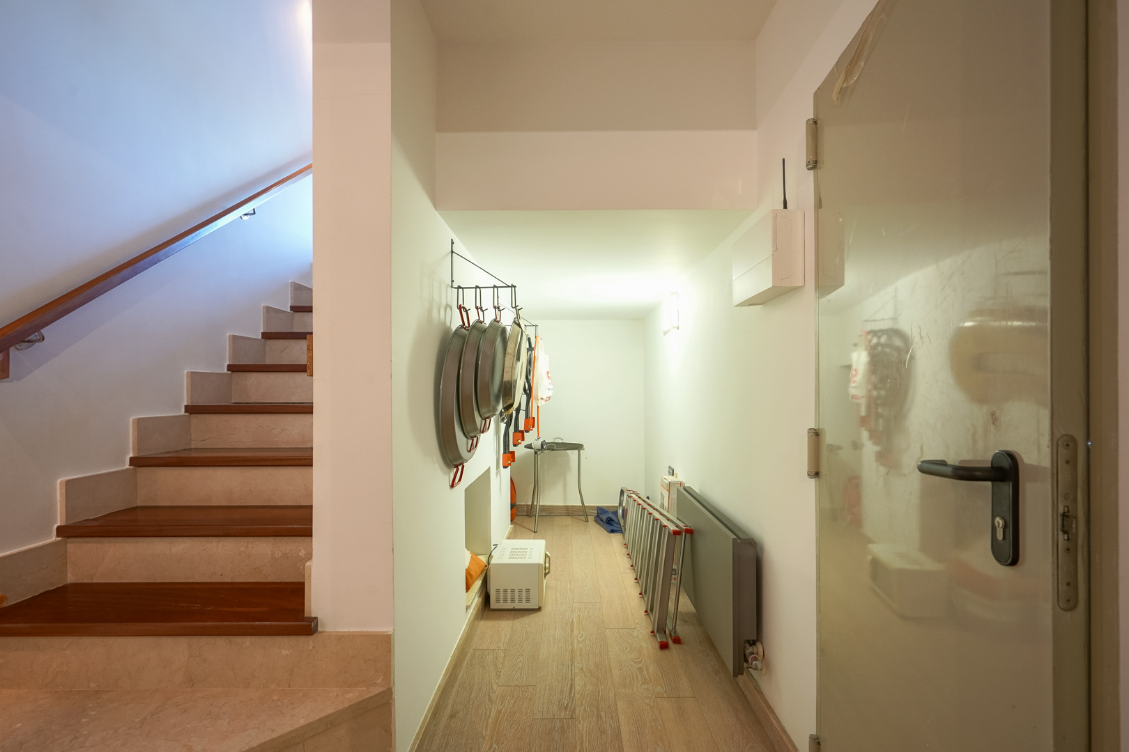 Pasillo de servicio con almacenaje para utensilios tradicionales, situado junto a una escalera de mármol y madera con pasamanos integrado.