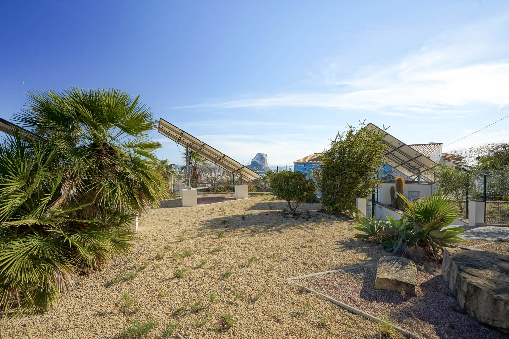 Sistema fotovoltaico con torres solares motorizadas en un jardín de grava, con vistas despejadas al Peñón de Ifach y vegetación mediterránea.