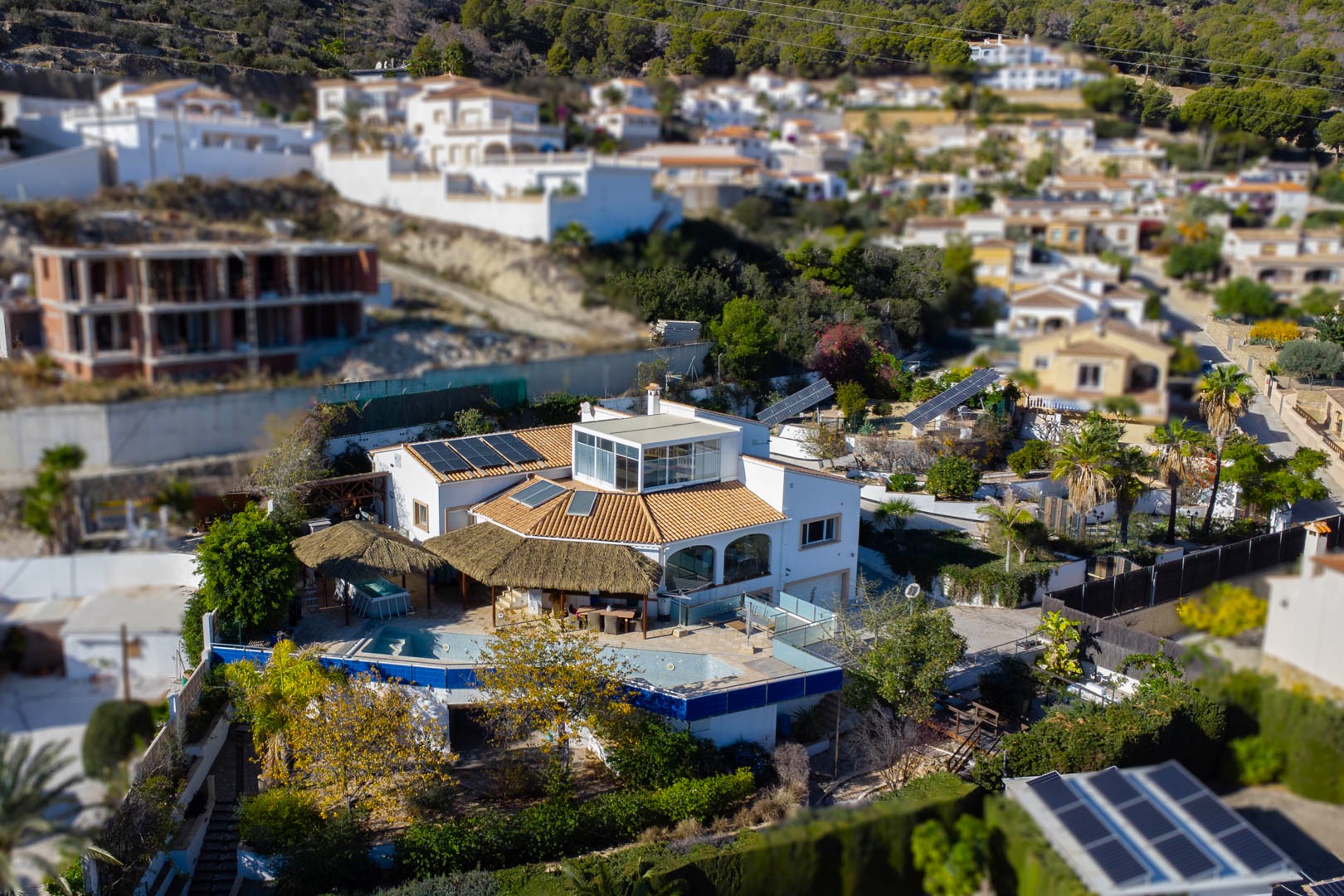Vista aérea de la villa que muestra la zona de piscina con pérgolas de brezo, el sistema de paneles solares en cubierta y seguidores solares motorizados en el jardín.