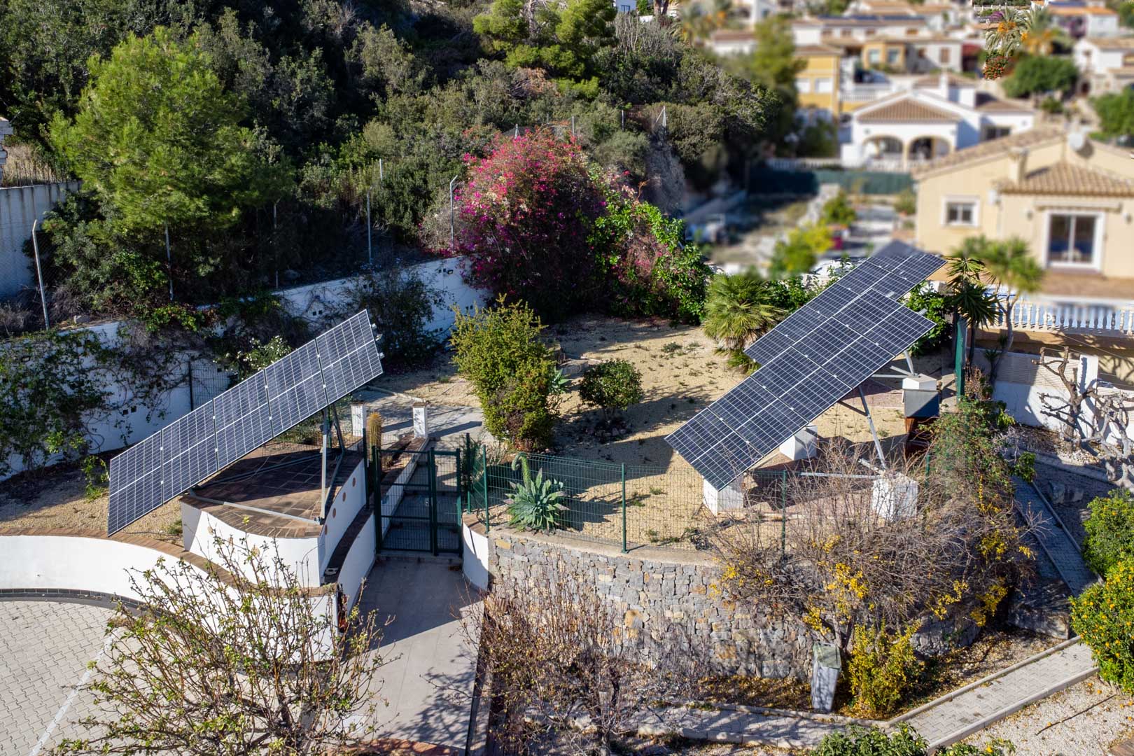 Vista aérea del sistema fotovoltaico con tres torres solares motorizadas instaladas en la parcela, rodeadas de vegetación mediterránea y muros de piedra natural.