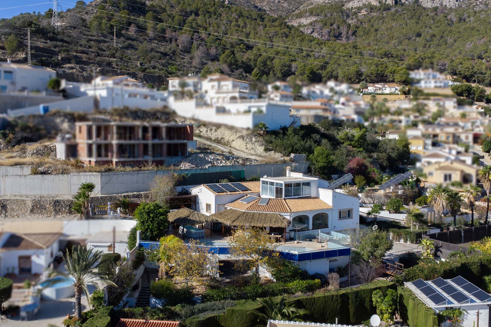 Vista exterior de la villa con arquitectura multinivel, paneles solares fotovoltaicos, terrazas con pérgolas de brezo y cerramiento acristalado superior en la ladera de Calpe.