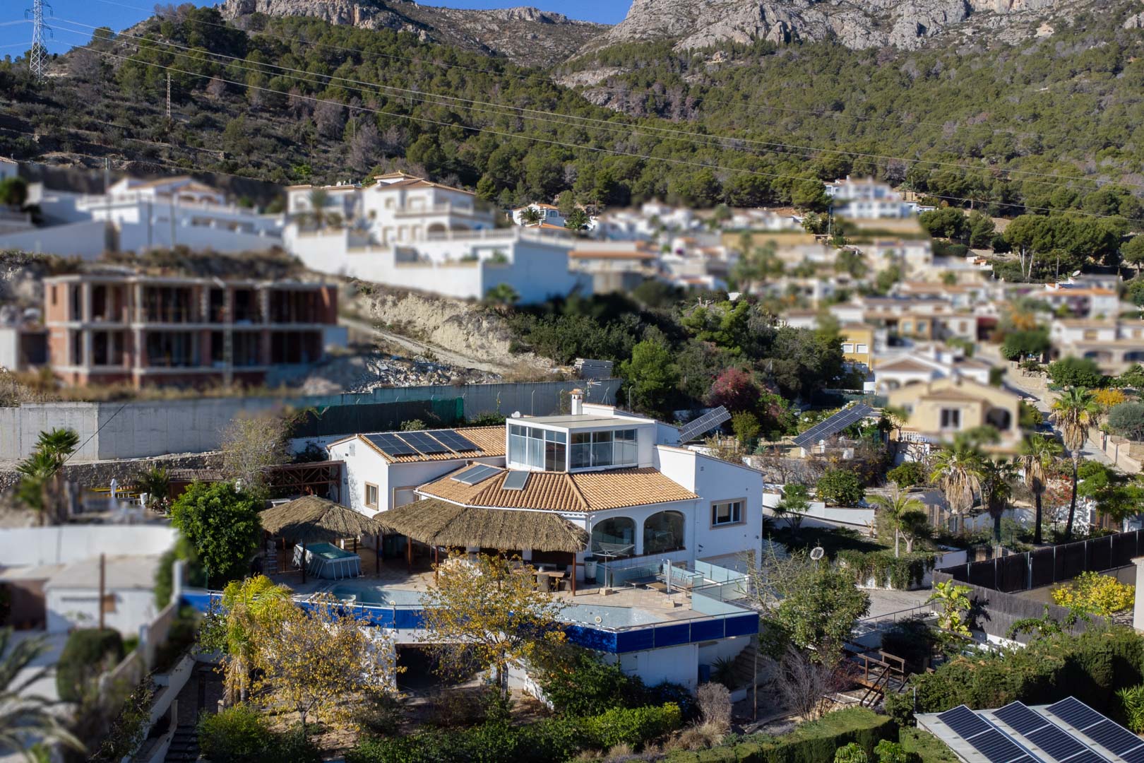 Vista exterior de la villa con paneles solares, terraza superior acristalada y zona de piscina con pérgolas de brezo bajo la Sierra de Oltamar.