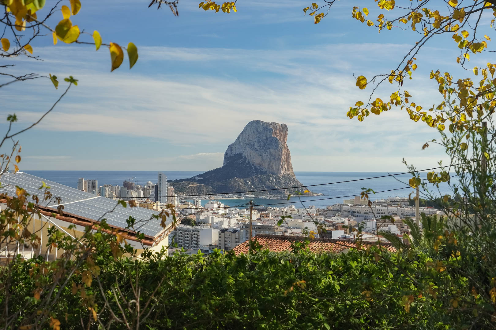 Vista panorámica del Peñón de Ifach y el skyline de Calpe desde la propiedad, destacando la instalación de paneles solares en la cubierta rodeada de vegetación.