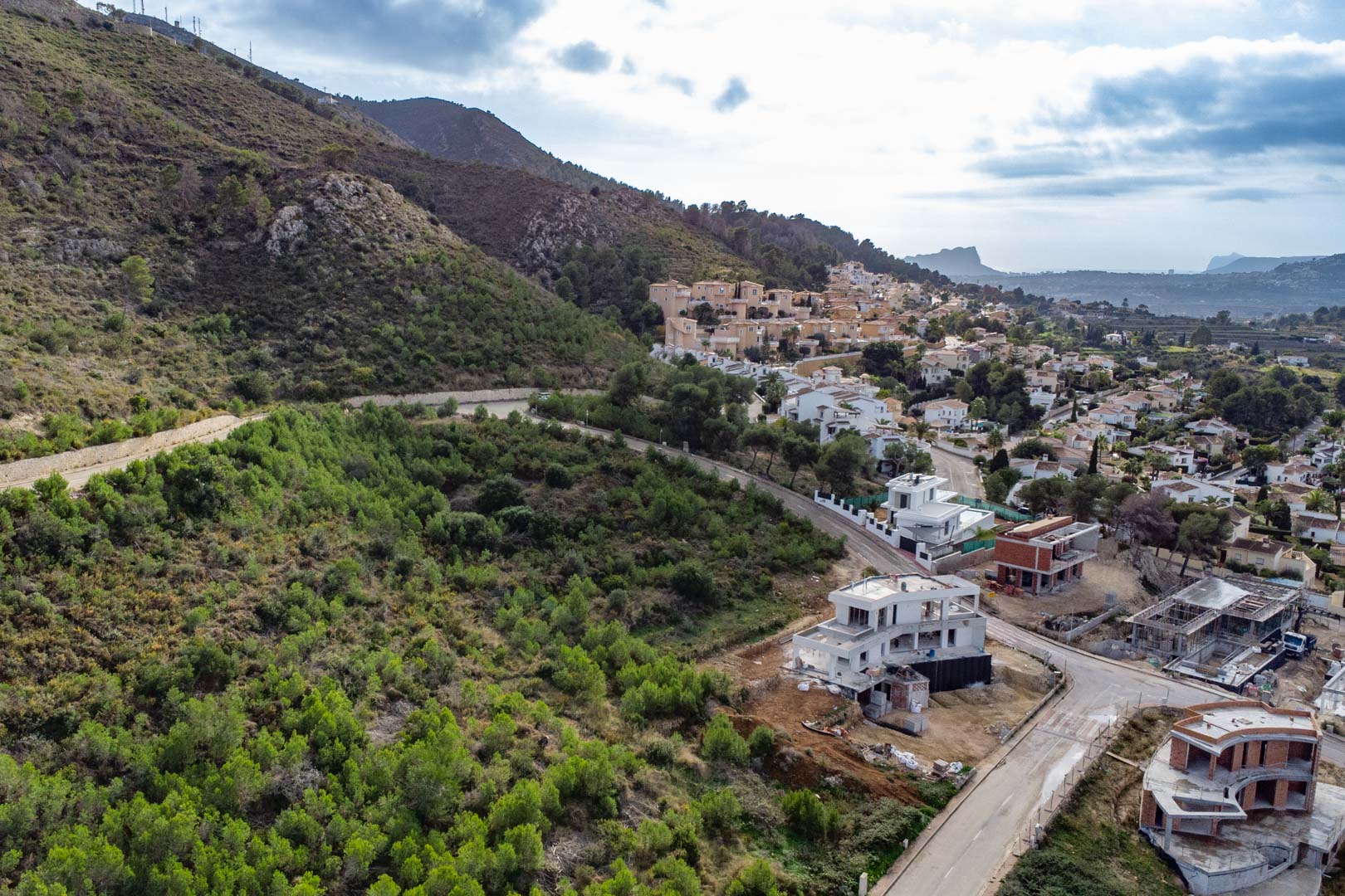 Vista aérea de la parcela elevada en Monte Olímpico, mostrando la infraestructura urbana, villas en construcción y el entorno natural de pinos con vistas al valle.