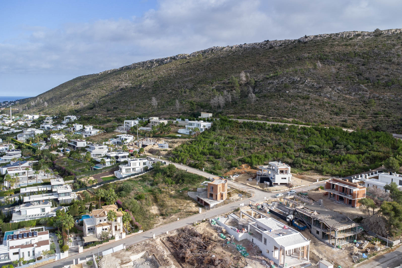 Vista aérea de la urbanización Monte Olímpico, mostrando parcelas con infraestructuras completas, viales asfaltados y villas de diseño moderno bajo la ladera.