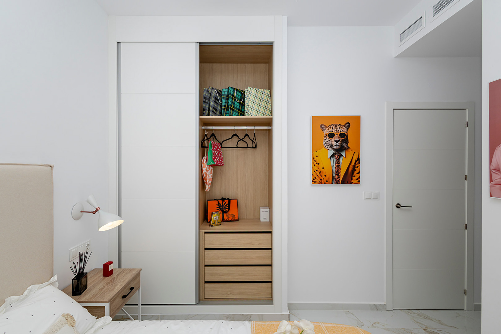 Dormitorio con armario empotrado de puertas correderas blancas e interior de madera. Incluye suelos de gres efecto mármol y sistema de aire acondicionado por conductos.
