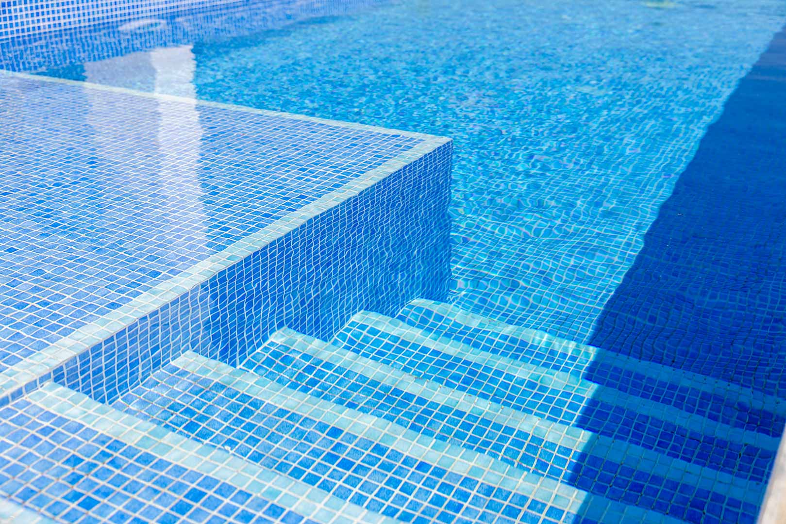 Primer plano de la piscina privada con revestimiento de gresite azul, destacando los escalones de obra sumergidos y la claridad del agua.