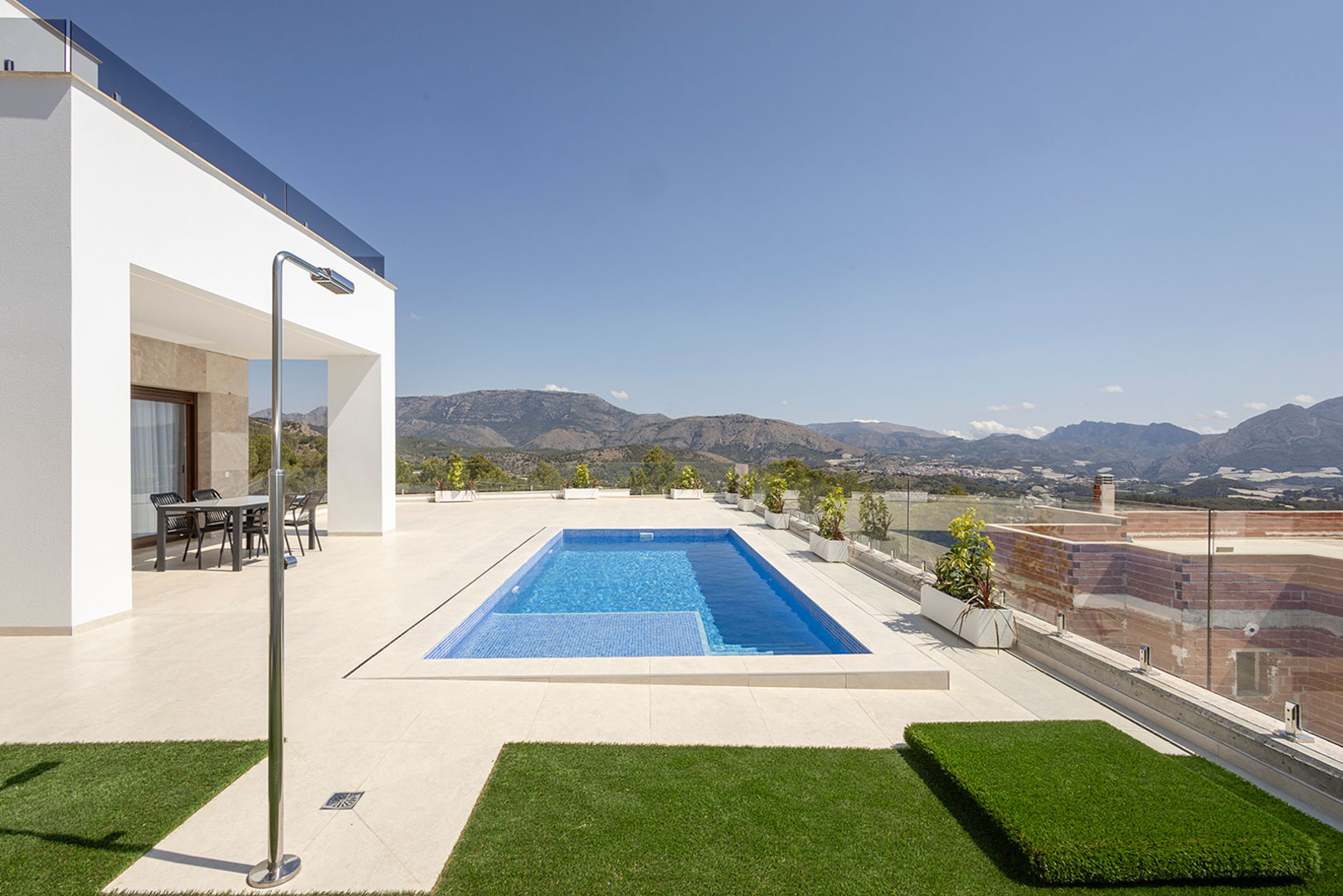 Terraza exterior con piscina privada, ducha de acero inoxidable y zona de comedor bajo porche, ofreciendo vistas panorámicas a las montañas y barandillas de cristal.