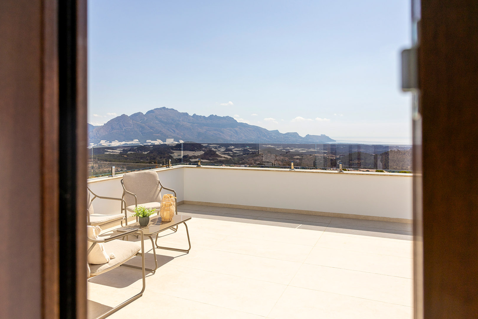 Terraza superior con barandilla de cristal, mobiliario de diseño y vistas panorámicas ininterrumpidas a las montañas y al mar Mediterráneo.