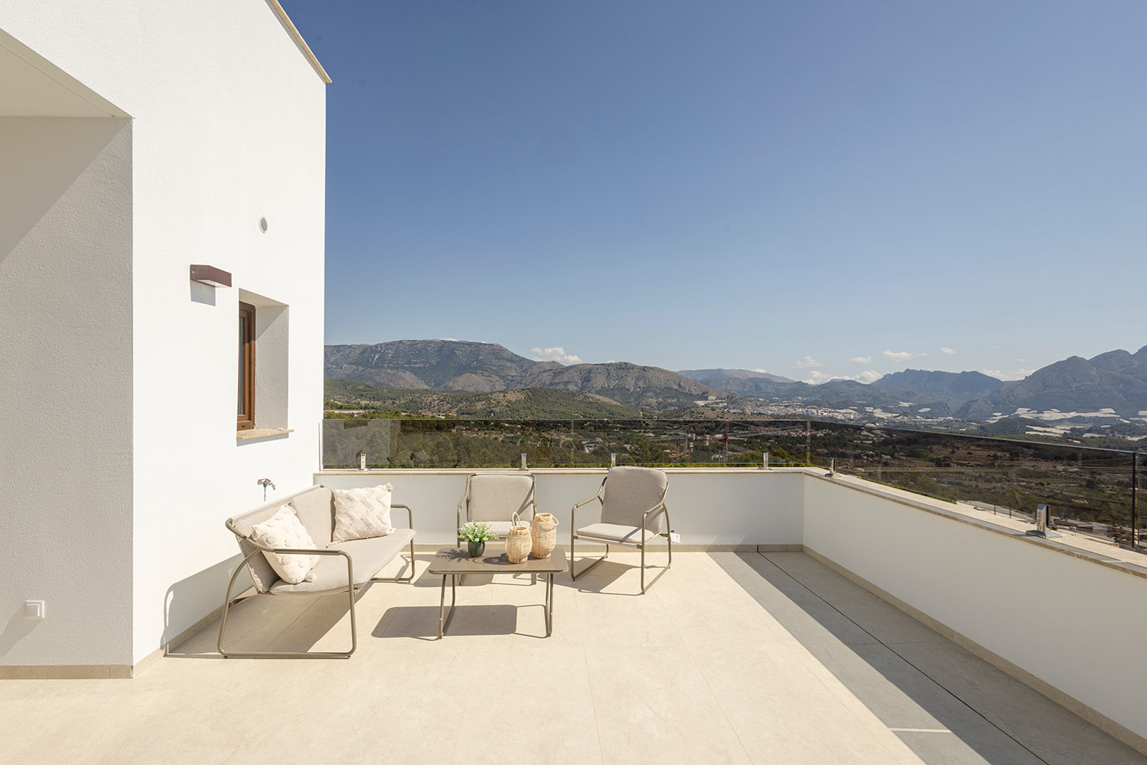Terraza superior con barandilla de cristal y zona de estar exterior, ofreciendo vistas panorámicas despejadas hacia las montañas y el entorno natural.
