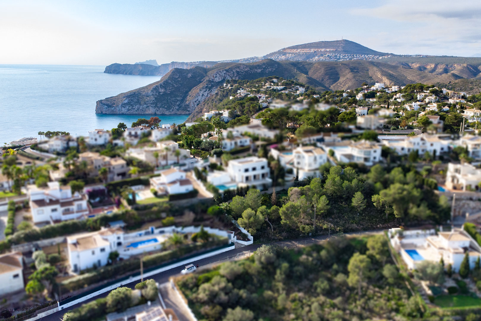 Vista aérea con efecto miniatura de la zona residencial Granadella-Ambolo, destacando las villas blancas y la costa escarpada de Jávea.