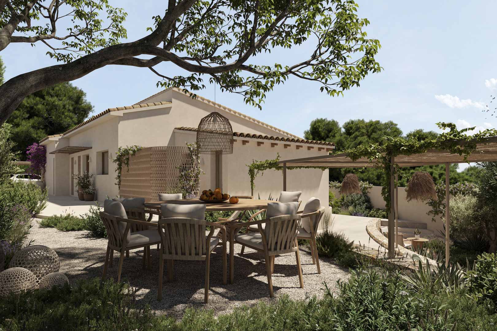 Comedor exterior con mesa circular de madera y sillas de fibras naturales sobre suelo de grava, integrado en un jardín mediterráneo con pérgolas y vegetación.