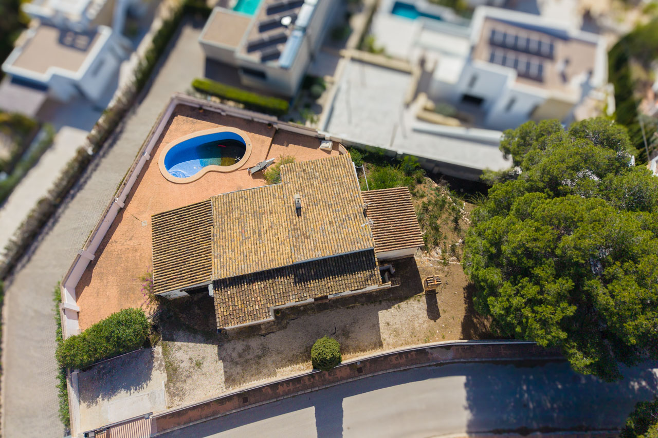 Vista aérea de la villa que muestra la cubierta de teja cerámica, la piscina de forma orgánica y la amplia parcela llana en una zona residencial consolidada.