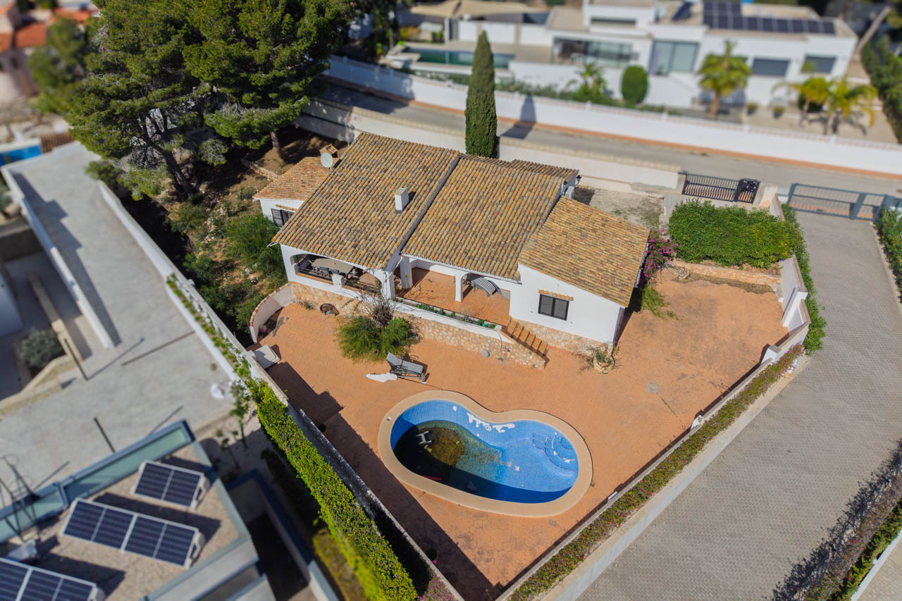 Vista aérea de la villa que muestra la parcela llana, la piscina de forma orgánica y la arquitectura mediterránea con tejados de teja cerámica y amplias terrazas.