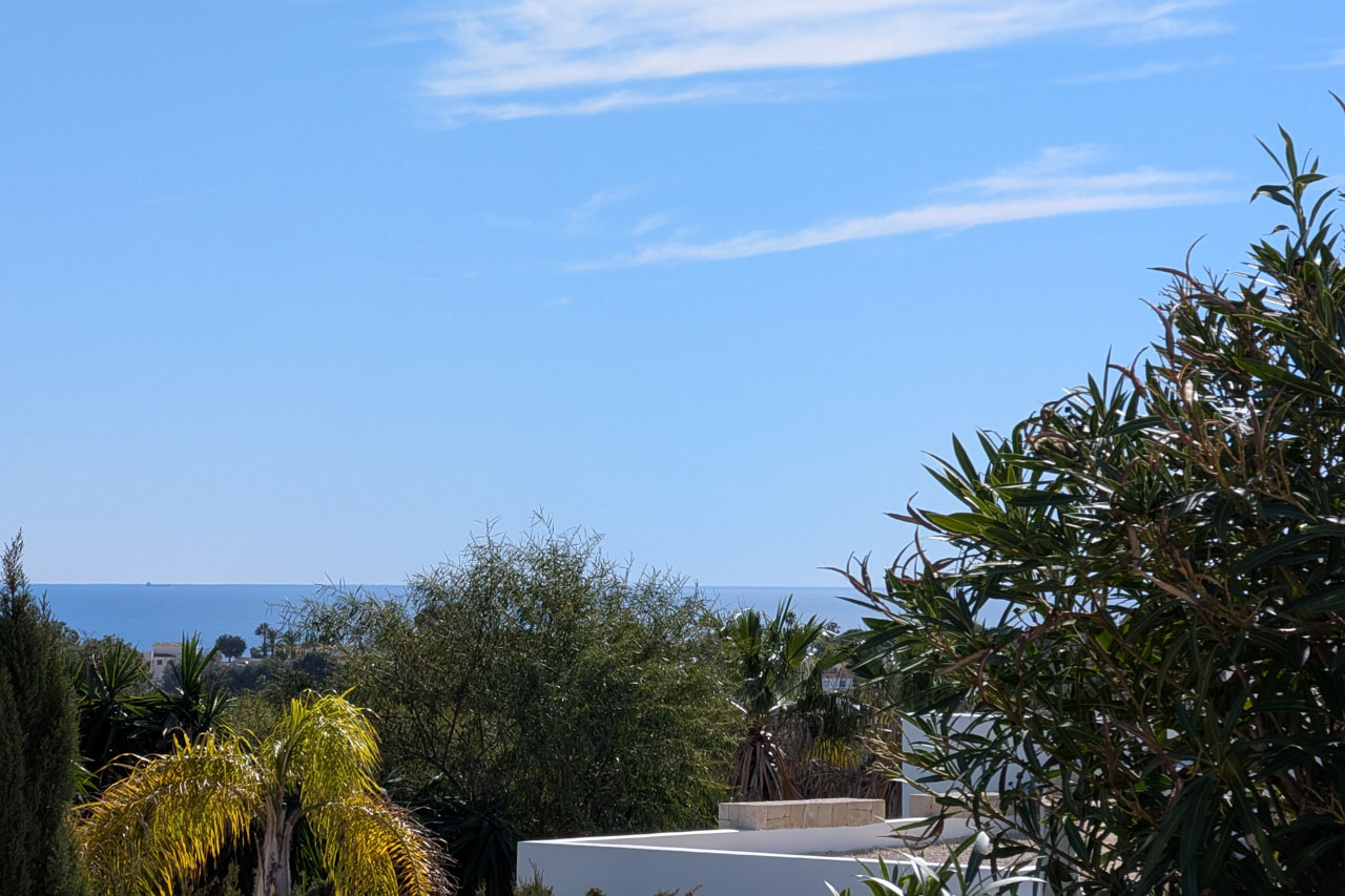 Vistas despejadas al mar Mediterráneo desde la propiedad, enmarcadas por vegetación autóctona y palmeras bajo un cielo azul en Benissa Costa.