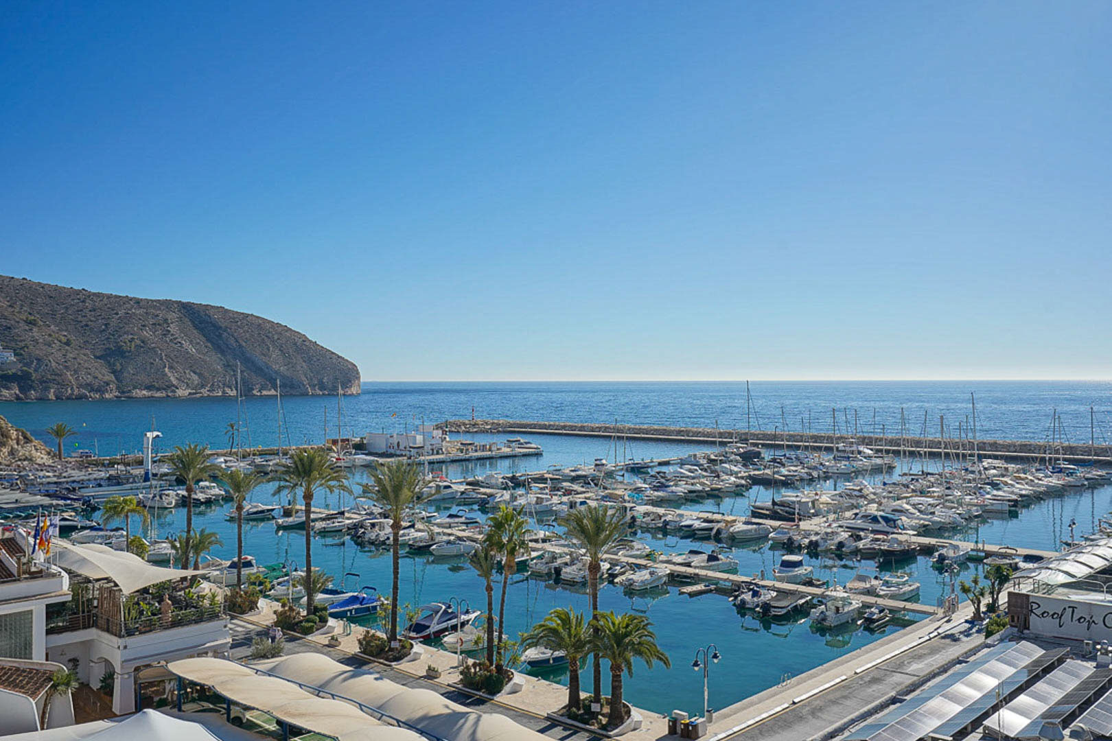 Vista panorámica del puerto deportivo de Moraira con el Cap d'Or al fondo, destacando la proximidad de la parcela a las instalaciones náuticas y al mar Mediterráneo.