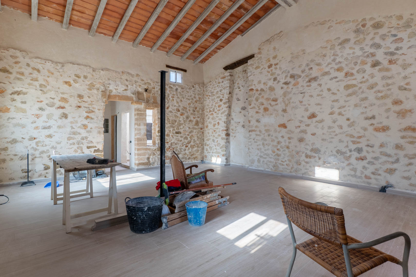 Estancia principal con paredes originales de piedra seca, techos altos de vigas de madera con bovedillas y suelos renovados que resaltan el carácter rústico de la finca.