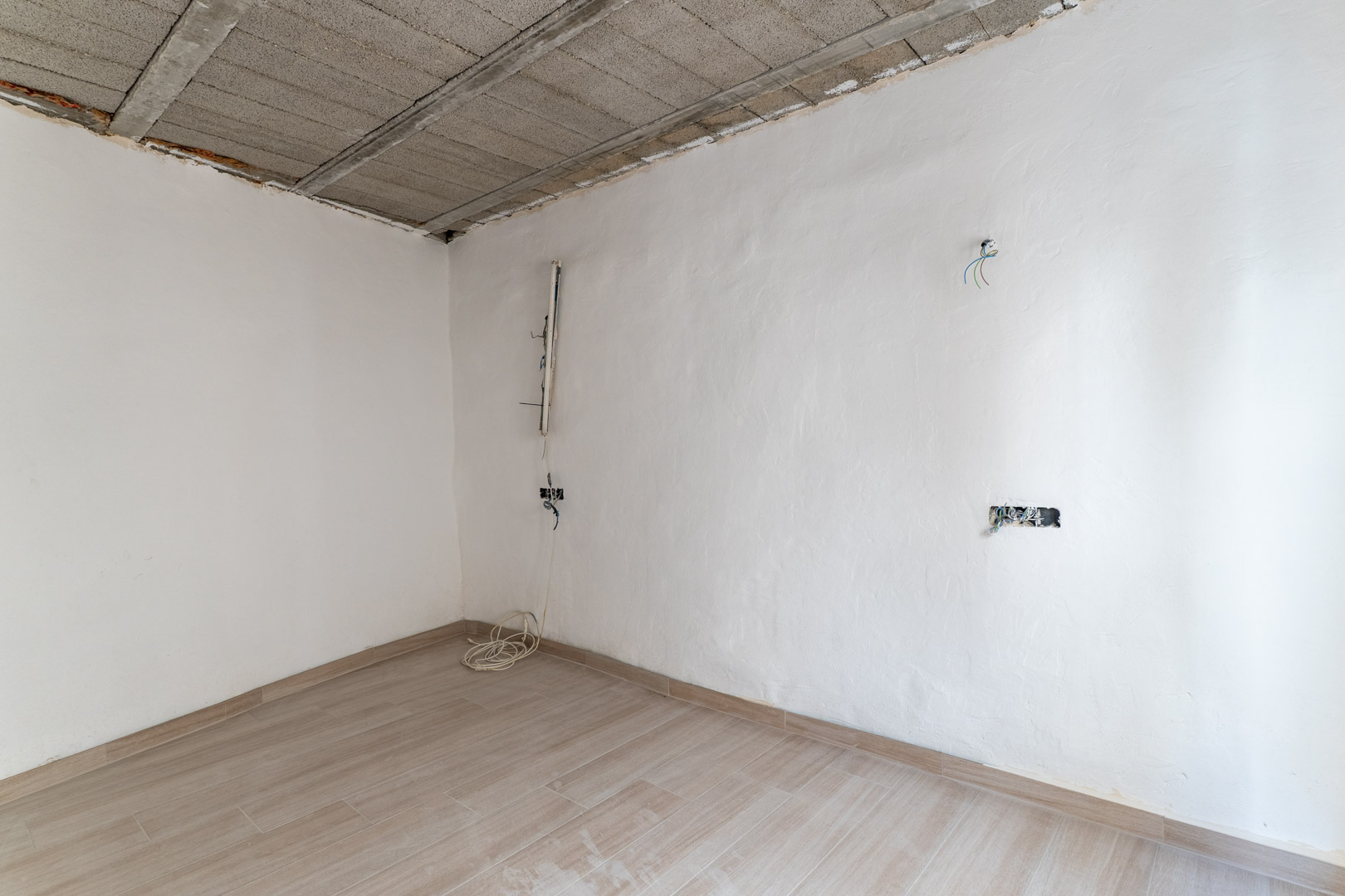 Habitación en proceso de reforma con suelos de gres efecto madera, paredes blancas y techo de viguetas de hormigón con preinstalación eléctrica.