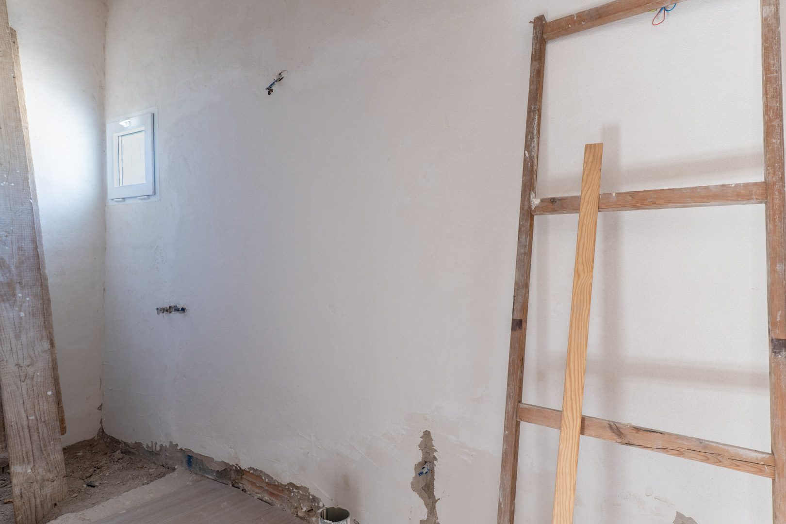 Habitación interior en fase de reforma con paredes recién enlucidas, ventana oscilobatiente blanca y tomas eléctricas preparadas para su finalización.