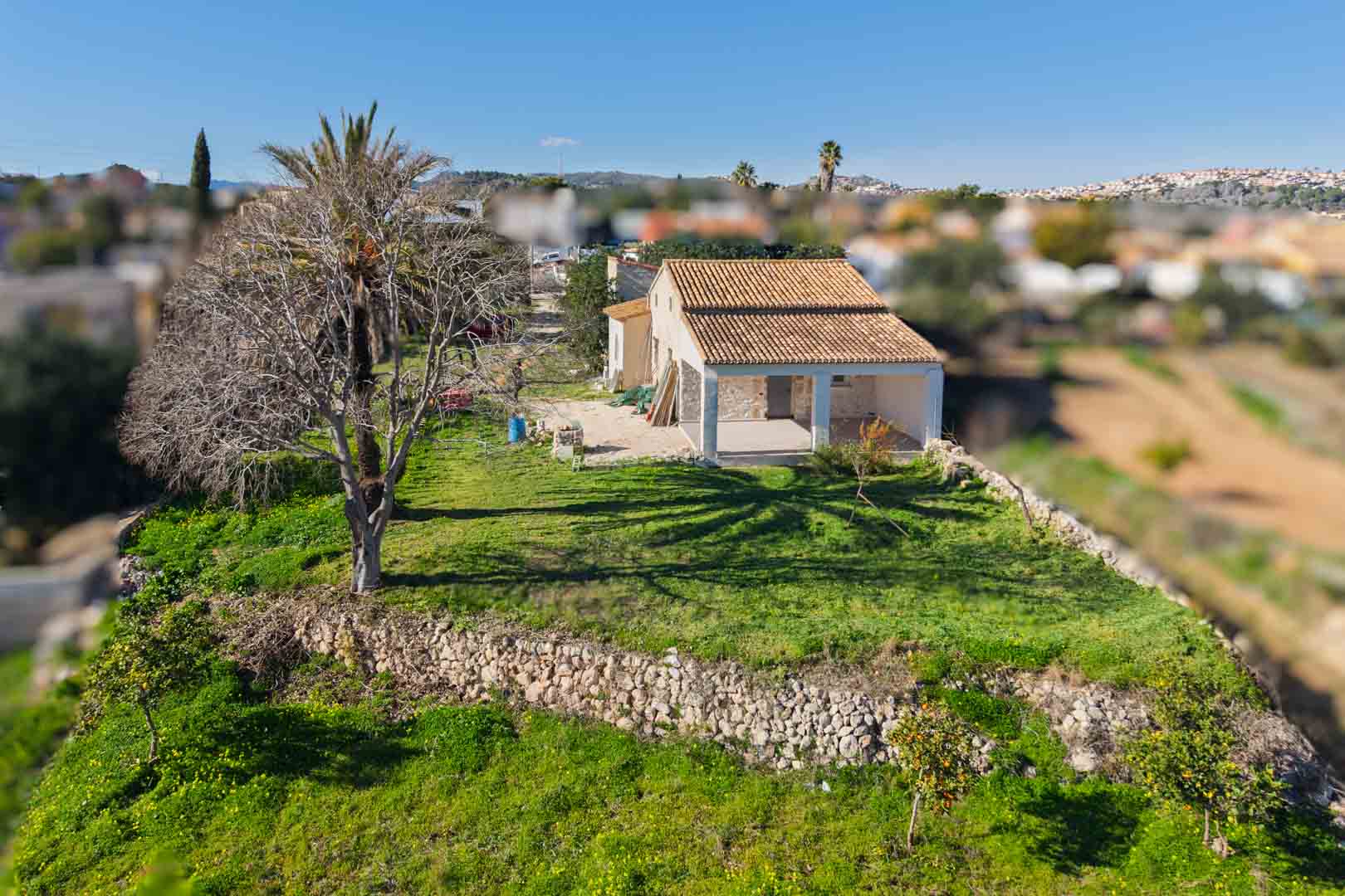 Vista aérea de la finca tradicional con tejado renovado, muros de piedra seca y una amplia naya, rodeada de vegetación y árboles frutales en Gata de Gorgos.