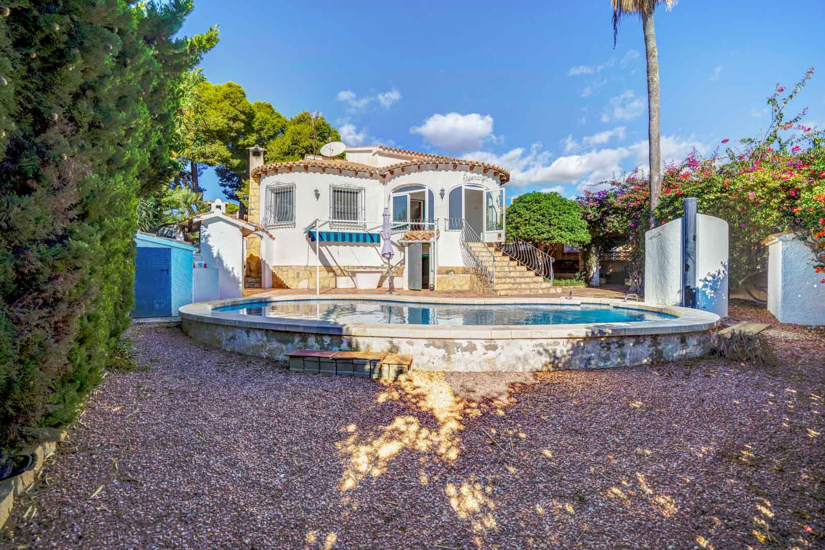 Fachada posterior de la villa con piscina privada elevada, jardín de grava y acceso por escaleras de piedra a la terraza acristalada superior.
