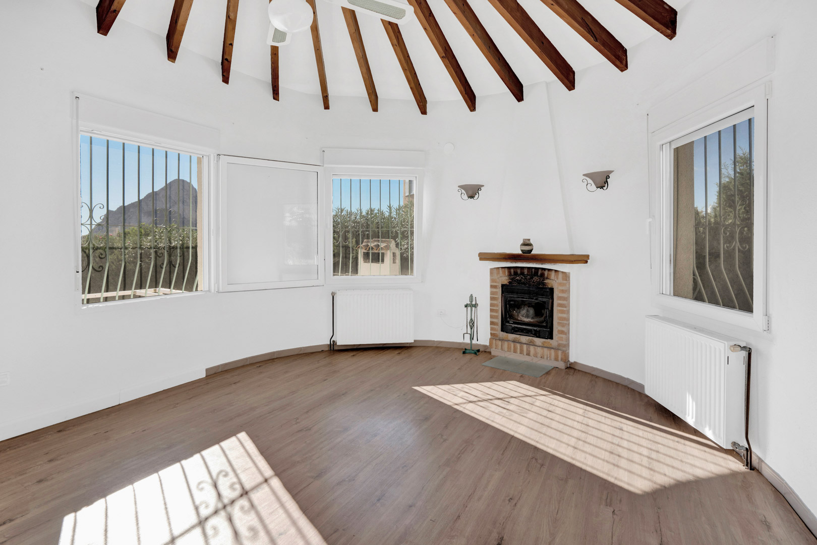 Salón circular con techos de vigas de madera radiales, chimenea de ladrillo y vistas directas al Peñón de Ifach a través de sus amplios ventanales.