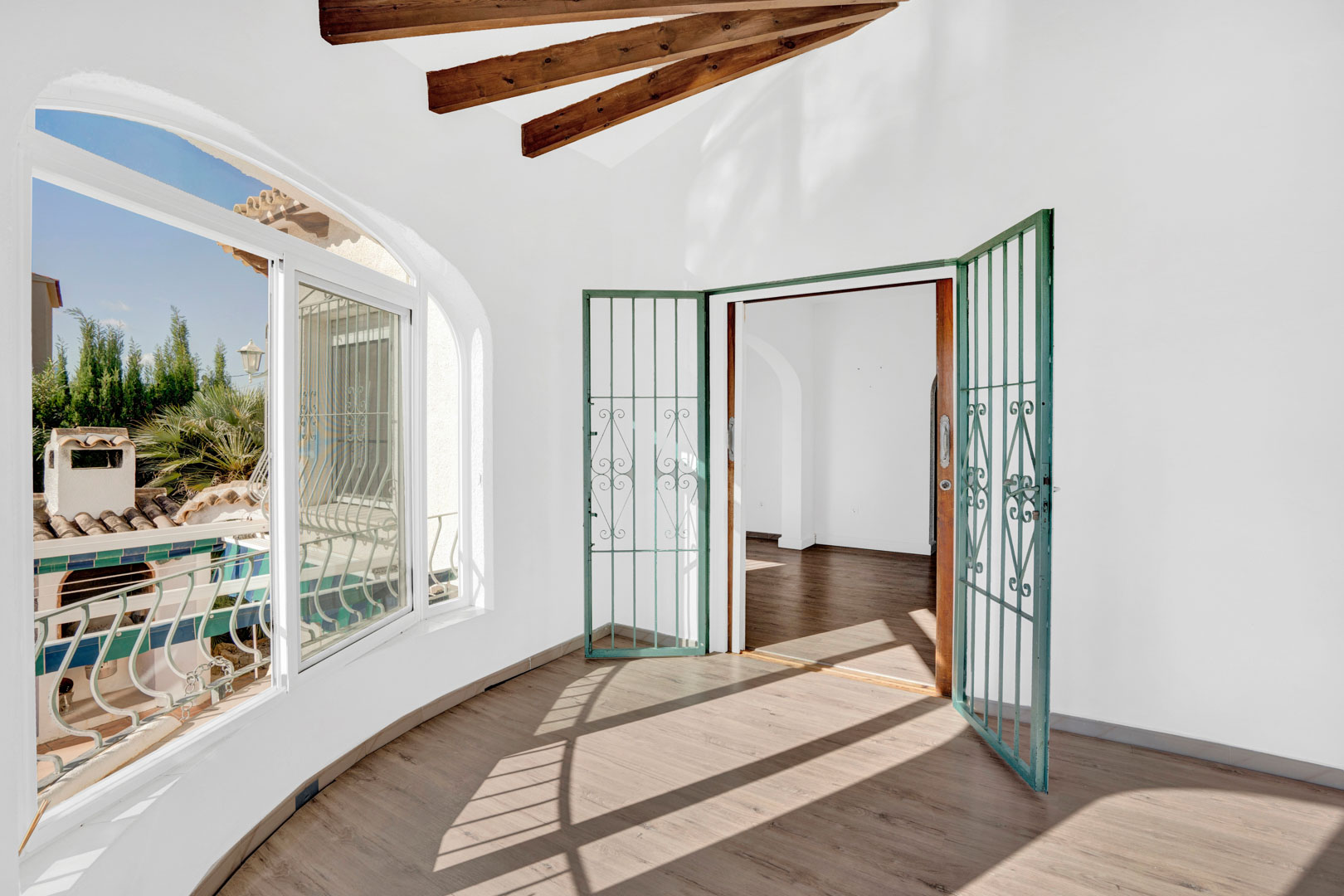 Terraza acristalada con vigas de madera decorativas, suelo laminado y ventanales en arco que aportan gran luminosidad y vistas al entorno exterior.