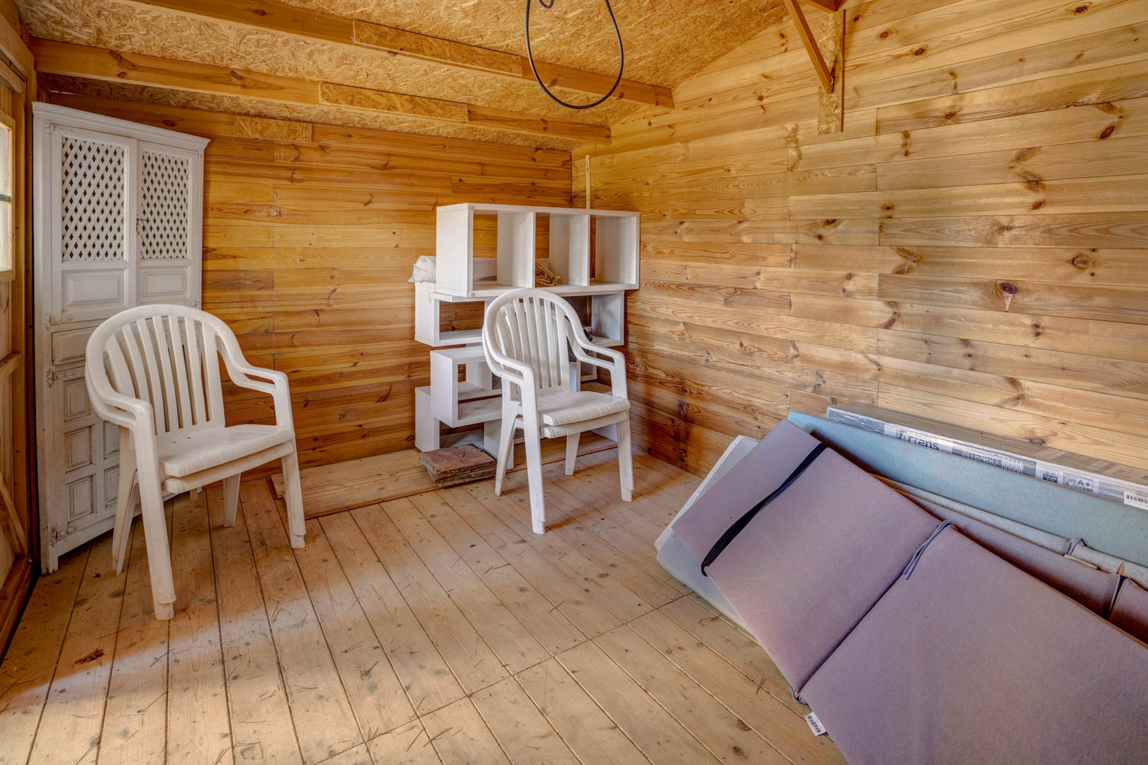 Trastero independiente con revestimiento integral de madera en paredes y suelos, proporcionando un espacio de almacenamiento funcional y seco con luz natural.