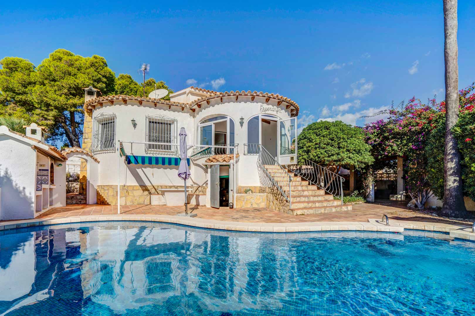 Vista exterior de la villa con piscina privada, fachada blanca de líneas curvas y escalera de piedra que da acceso a la terraza acristalada superior.